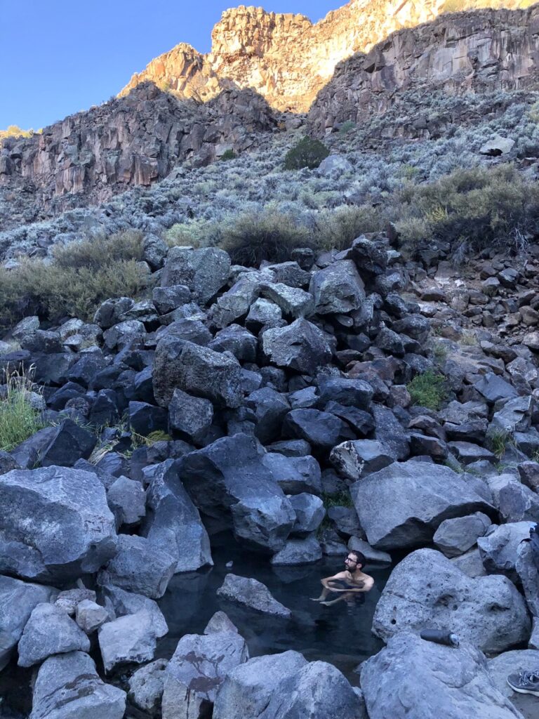 Jonathan sits in a hot spring surrounded by black rocks. 