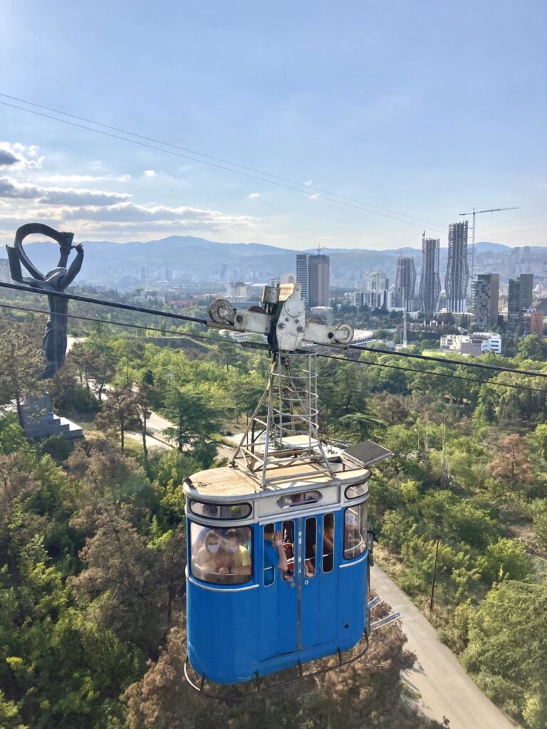 a blue and white old cable car takes passengers up on a wire cable line. city buildings in background. 