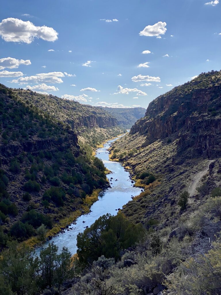 top 7 things to do in Taos. a blue river is surrounded by brown canyon walls and the backdrop of a blue sky dotted with clouds. 