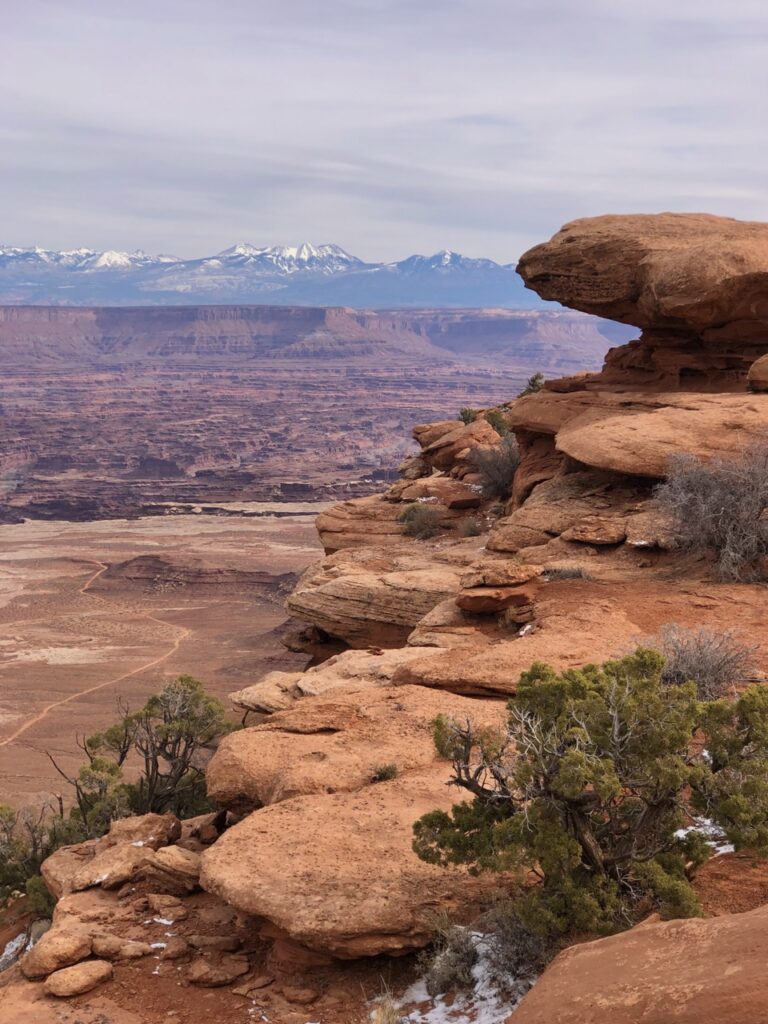 jagged red rocks, green sage brush and distant hazy canyon. how to spend a weekend in moab, utah.