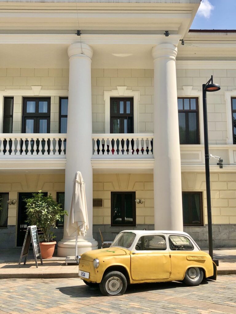 white columned building behind a bright yellow and white vintage car. 10 awesome things to do in Tbilisi, georgia 