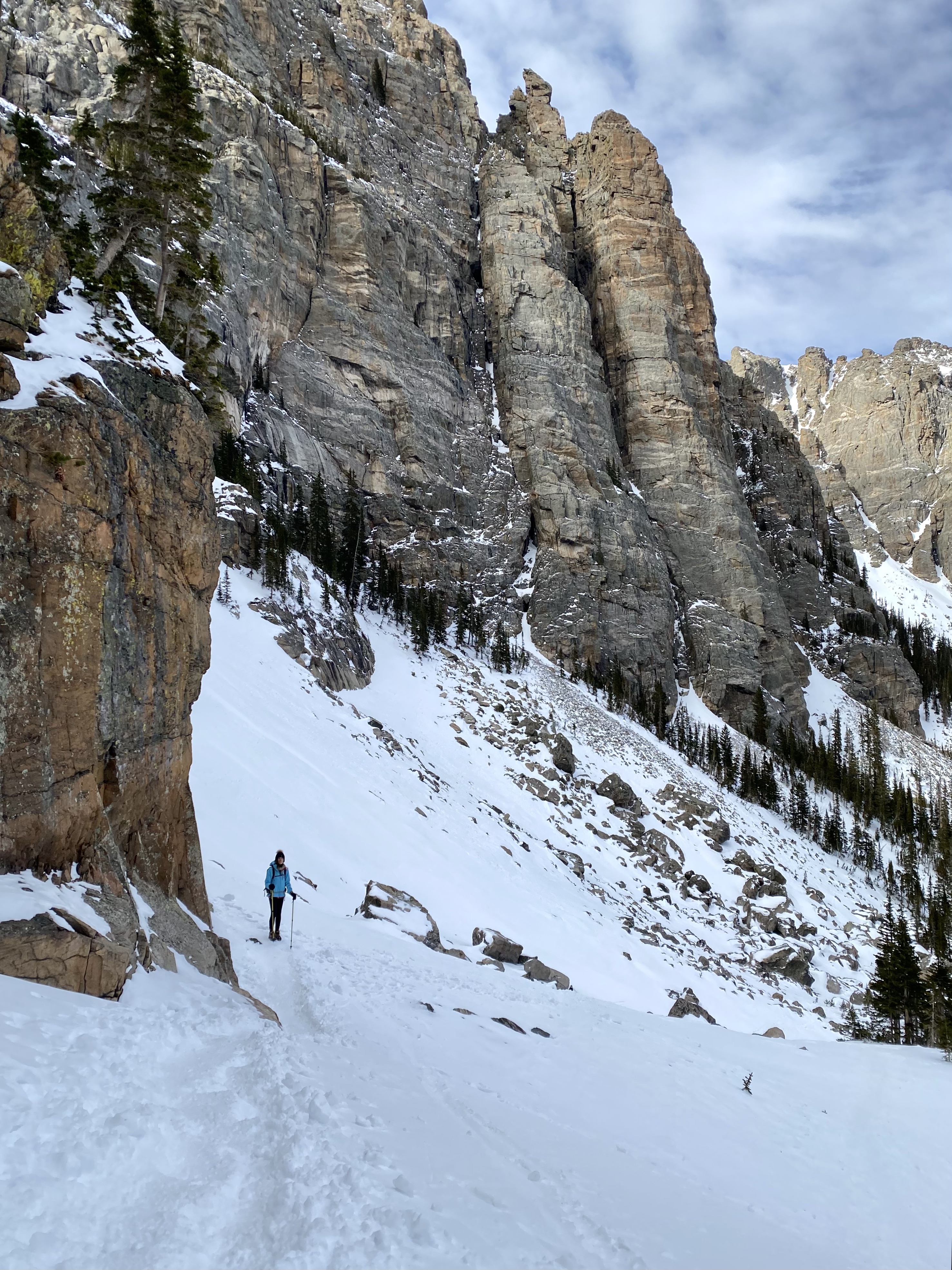 Sky Pond Trail in Rocky Mountain, towering rock formations and small hiker on snow covered ground