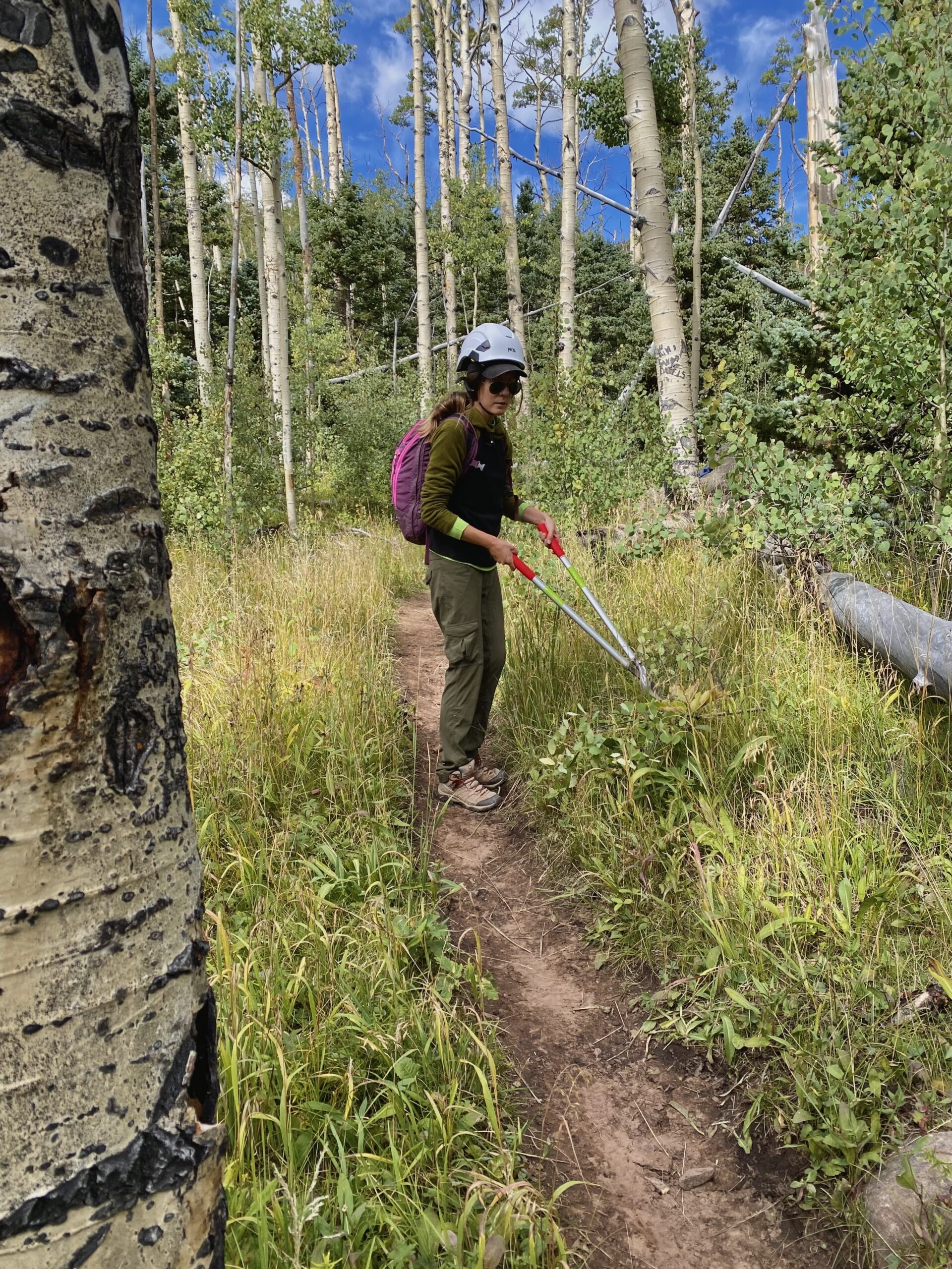 outdoor volunteer opportunities - caroline works on a trail with green pants and green sweater and a hard hat on. 