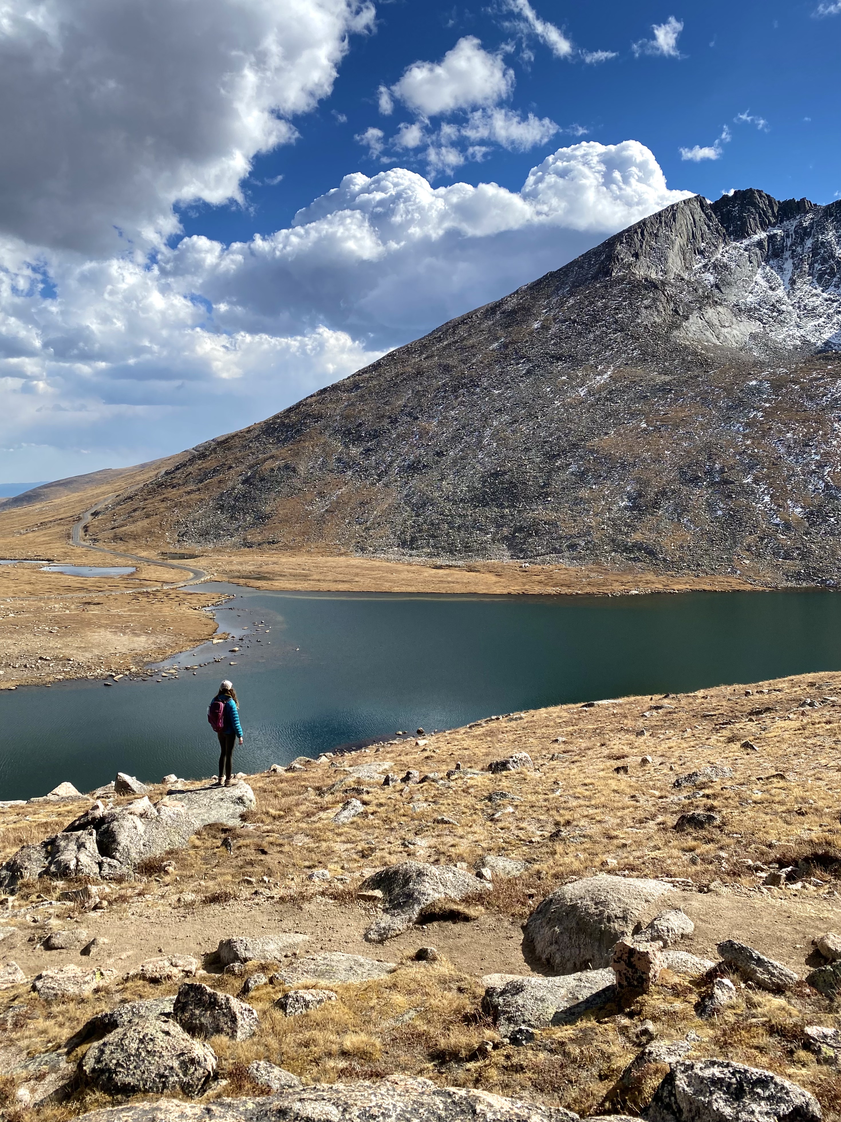 blue sky with clouds and mountain and lake backdrop, tiny hiker