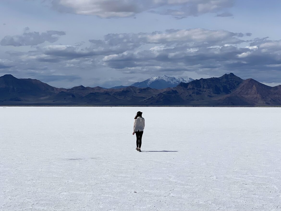Caroline walking on a white grounds (the salt flats) with distant brown mountains and blue sky backdrop.