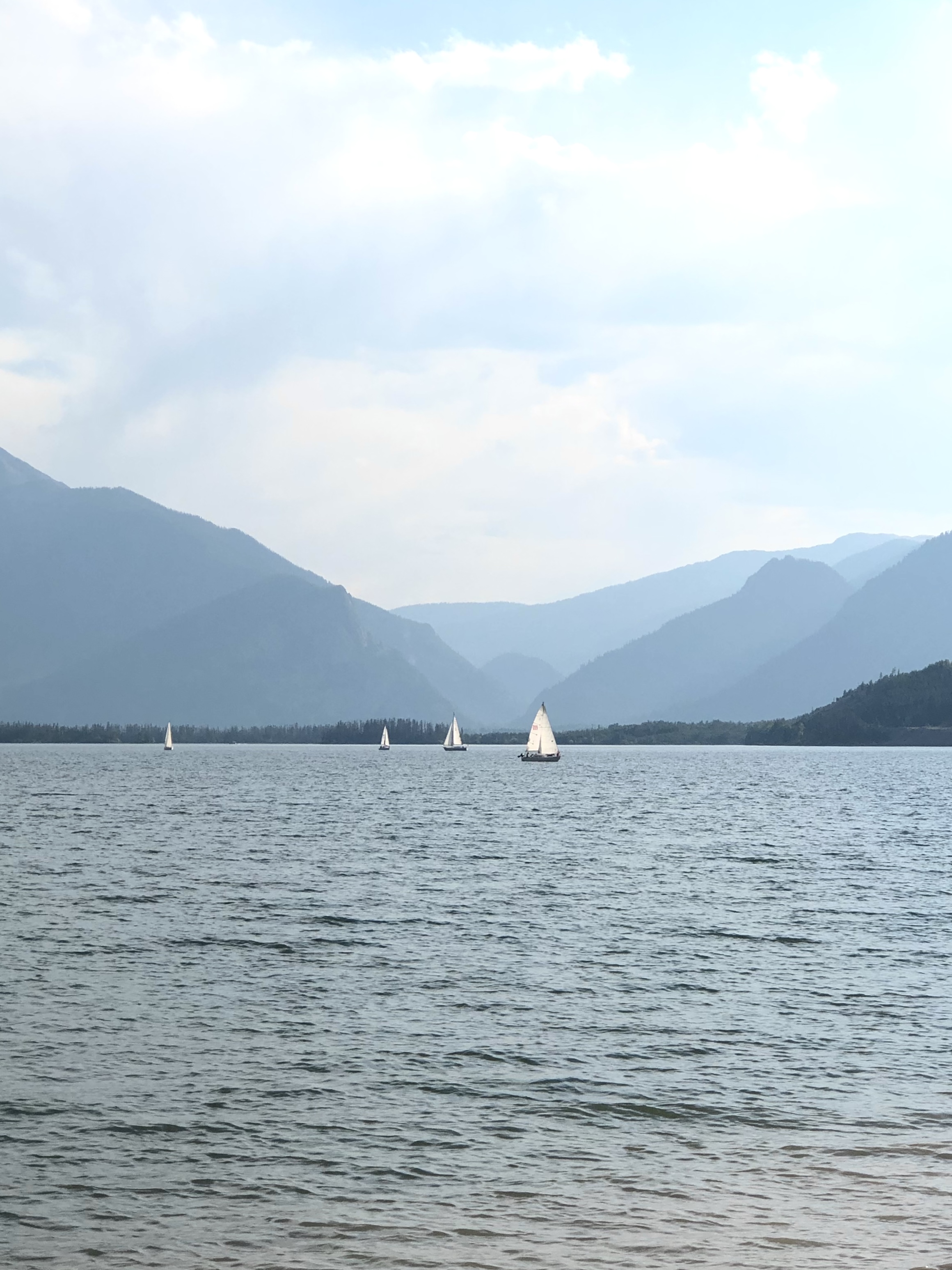 blue layers of mountains with tiny white sail sailboats on a blue lake. 10 beautiful spots to visit in colorado (no hiking required)