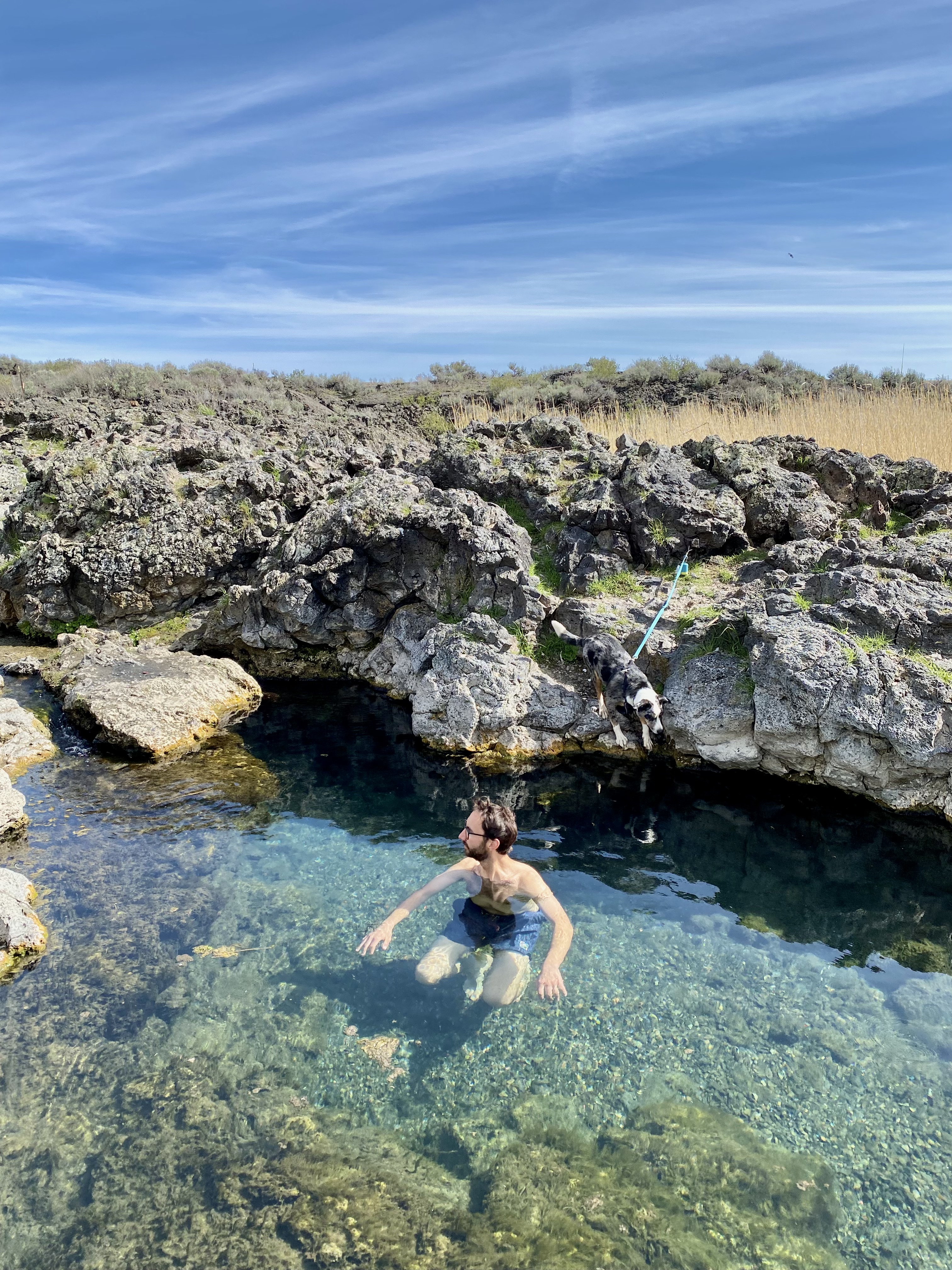 Jonathan swims in clear turquoise colored water surrounded by gray lava rocks. 