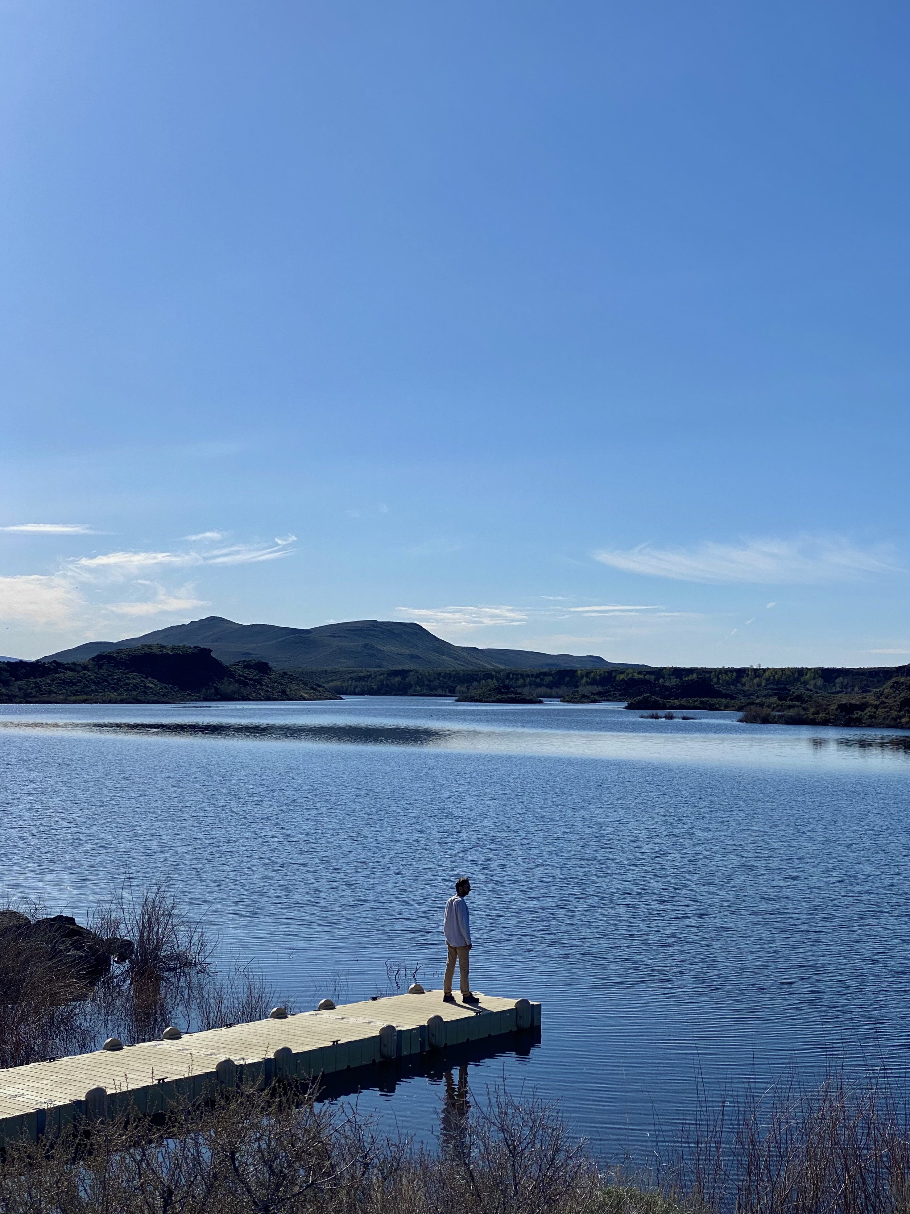 Jonathan, in a white shirt and tan pants, stands on a dock that extends into a blue lake. unique places to visit on a southern idaho road trip. 