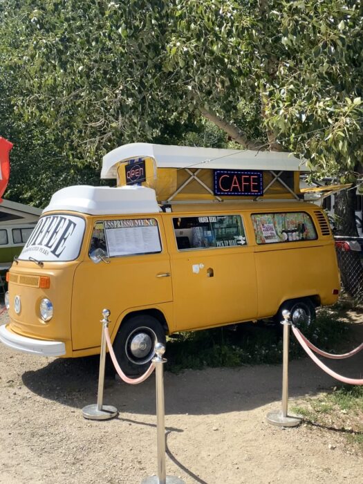 A yellow VW bus with a white top has been converted into a coffee shop with a cafe sign. 